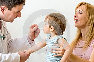 Doctor giving to child medicament with a spoon. Mother looking at
