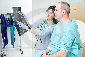Doctor in gloves and adult man looking MRI images in clinic