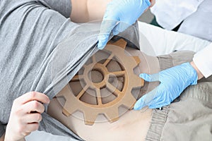 Doctor in gloves examining abdomen of patient with wooden gear closeup