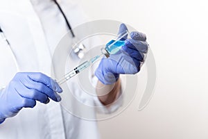 Doctor in gloves filling up syringe from bottle with vaccine, medicine