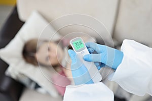 Doctor in gloves measuring temperature of woman with non contact thermometer at home closeup