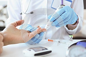 Doctor with gloves piercing patients finger with lancet closeup