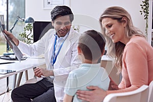 Doctor Or GP In White Coat Meeting Mother And Son For Appointment In Office