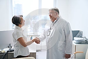 Doctor greets an elderly patient with handshake in medical office