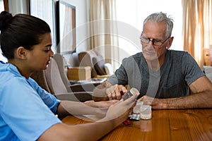 Doctor guiding senior man in taking medicine at table