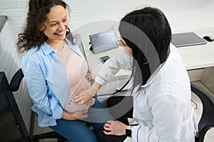 Doctor gynecologist listening to pregnant patient& x27;s belly. Happy woman visits obstetric clinic for pregnancy checkup