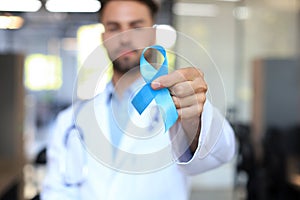 Doctor hand with blue prostate cancer awareness ribbon. Medicine oncology closeup sky symbol