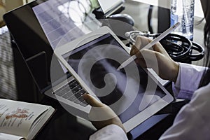 Doctor hand holding digital tablet with chest x-ray film CXR  on screen and work on laptop computer