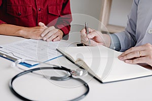 Doctor hand holding pen writing patient history list on note pad and talking to the patient about medication and treatment