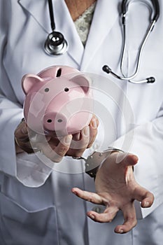 Doctor In Handcuffs Holding Piggy Bank Wearing Lab Coat, Stethoscope