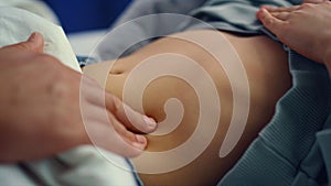 Doctor hands checking stomach of little sick girl in hospital ward closeup.