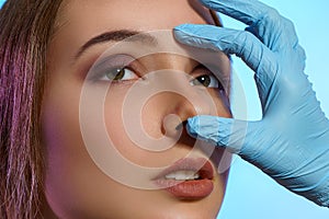 Doctor hands in medical gloves measure the nose with fingers on face of beautiful young girl. Clinic of Plastic Surgery