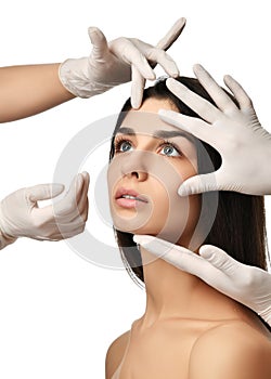 Doctor hands in medical gloves touch beautiful young woman face with closed eyes after plastic surgery