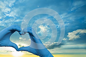 Doctor hands in medical surgical gloves making heart on sky clouds background