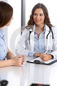 Doctor and happy patient talking while sitting at the desk. The physician or therapist discussing healthy lifestyle