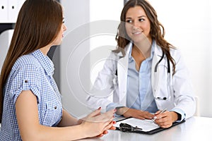 Doctor and happy patient talking while sitting at the desk. The physician or therapist discussing healthy lifestyle