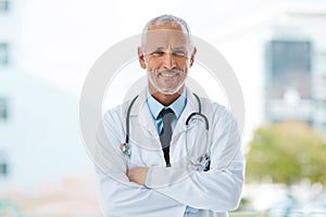 Doctor, happy and portrait of mature man in a hospital at a cardiology clinic with arms crossed. Professional, medical