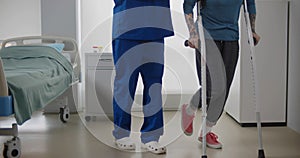 Doctor helping female patient in crutches at hospital ward