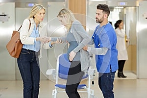 Doctor helping pregnant woman to sit down on wheelchair