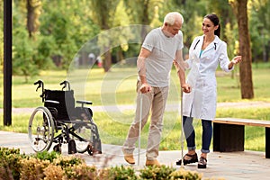 The doctor helps the patient to walk on crutches. Wheelchair left behind