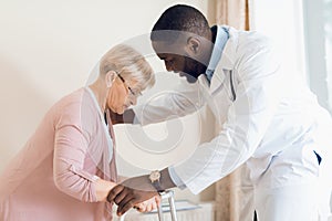The doctor helps to get out of bed an elderly woman in a nursing home.