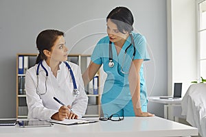 Doctor and her assistant working together at hospital. Physician and nurse with documents at medical office