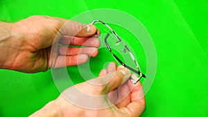 Doctor with his fingers demonstrates the eyepieces of glasses on a green background