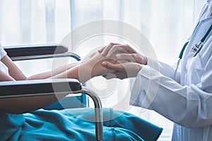 The doctor hold hands patient Which sat on wheelchair to encourage