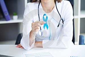 Doctor holding blue awareness ribbon at her office