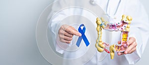 Doctor holding Blue ribbon with human Colon anatomy model. March Colorectal Cancer Awareness month, Colonic disease, Large
