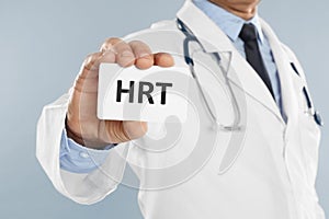 Doctor holding card with abbreviation HRT on light grey background, closeup. Hormone Replacement Therapy photo