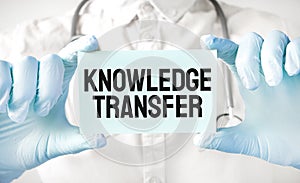 Doctor holding card in hands and pointing the word KNOWLEDGE TRANSFER