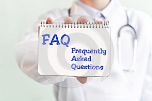 Doctor holding a card with text FAQ Frequently Asked Questions medical concept