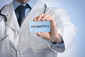 Doctor holding card with word PREBIOTICS on light blue background, closeup photo