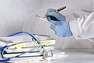 Doctor holding clipboard and writing a prescription, stack of documents and books, stethoscope on the white desk