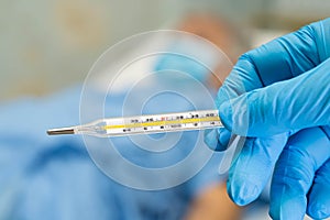 Doctor holding digital thermometer to measures asian senior or elderly old lady woman patient wearing a face mask have a fever