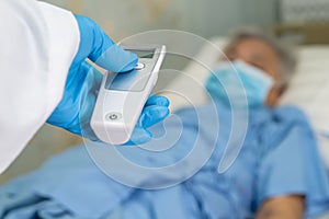 Doctor holding digital thermometer to measures asian senior or elderly old lady woman patient wearing a face mask have a fever.