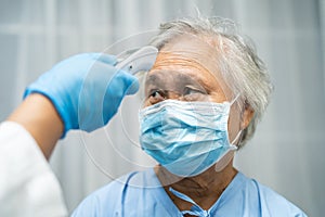 Doctor holding digital thermometer to measures asian senior or elderly old lady woman patient wearing a face mask have a fever in