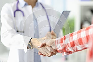 Doctor holding documents and shaking hands with patient in clinic close-up