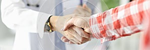 Doctor holding documents and shaking hands with patient in clinic close-up