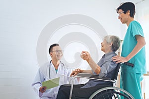 Doctor holding elderly patient `s hand in a wheelchai, giving su