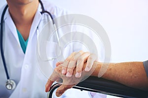 Doctor holding elderly patient `s hand in a wheelchai, giving su