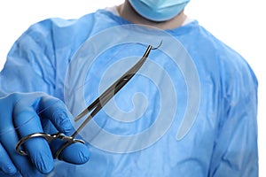 Doctor holding forceps with suture thread on white, closeup. Medical equipment
