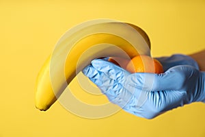 Doctor holding fruits symbolizing male sexual organ on yellow background, closeup. Potency problem