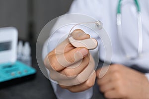 Doctor holding hearing aid against blurred background