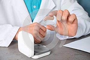 Doctor holding hearing aid at table, closeup.