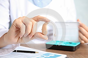 Doctor holding hearing aid at table, closeup.