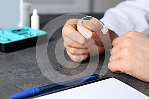 Doctor holding hearing aid at table, closeup Medical objects