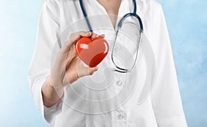 Doctor holding heart model on light background. Cardiology service