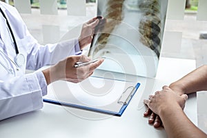 Doctor holding and looking at x-ray film examining at lungs radiograph of patient chest injury and analyze result while discussing